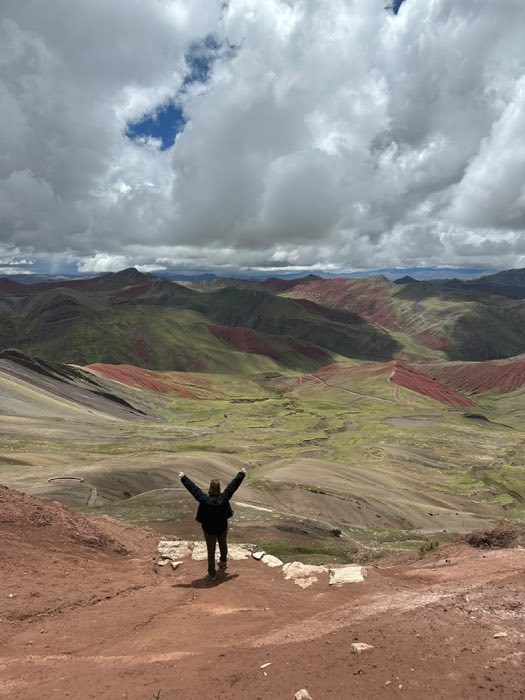 Annette Serio Haddad with arms raised at Vinicunca Rainbow Mountain, Peru